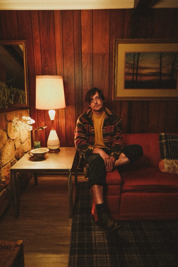 Jonathan Sexton seated on a red couch, a lamp glowing beside him.